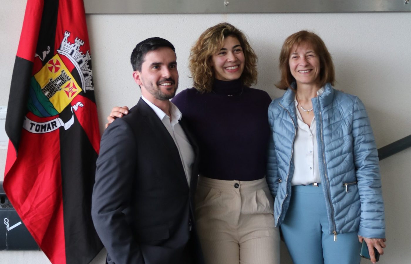 Três pessoas junto à placa do Pavilhão Municipal Patrícia Sampaio, em Tomar